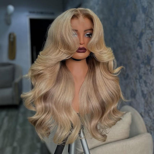 A mannequin in a salon setting showcases NuHaire's Ash Blonde Ombre Layered Cut Loose Wave Wig, featuring a brown root that blends into ash blonde highlights. This 250% density human hair wig offers a layered cut, loose wave texture, and various transparent lace size options for a natural hairline.