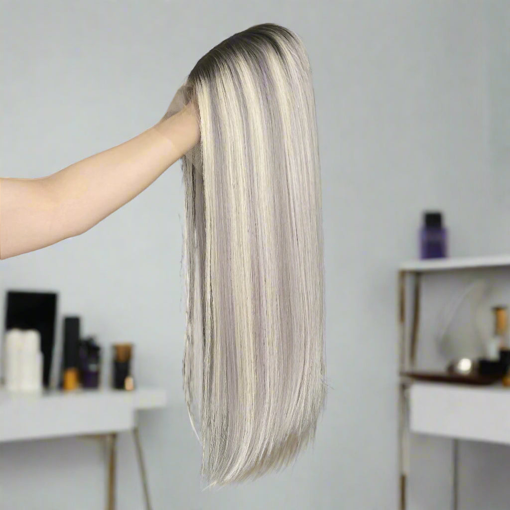 Person holding European human hair glueless long, straight hair wig in a room with white walls and shelves.