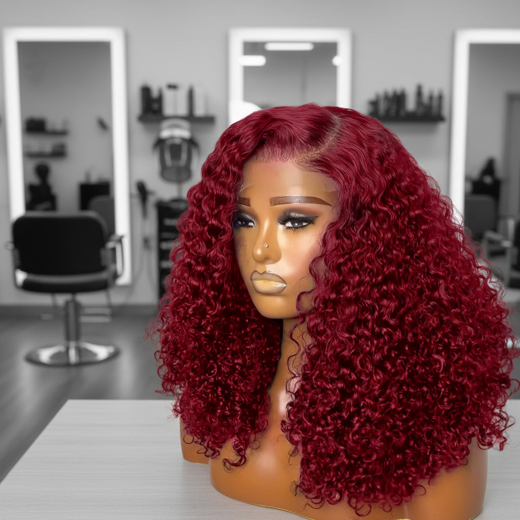 Mannequin head featuring a NuHaire burgundy pixie curly wig, showcasing rich burgundy 99J color, with bouncy, combed-out pixie curls and thin transparent lace options available in 4x4 and 13x4.