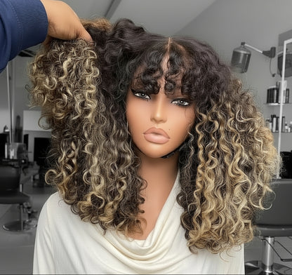 The mannequin showcases NuHaire's Honey Blonde Balayage Highlight Afro Kinky Curly Wig with Bangs, featuring a dark brown base with honey blonde highlights, a kinky curly texture, made from premium human hair, and designed with a glueless 5x5 lace.