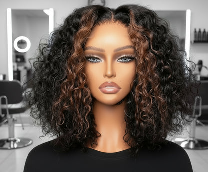 Front view of Mannequin head featuring NuHaire's Caramel Blonde Highlight Curly Bob Wig, showcasing a flawless caramel blonde highlight, premium human hair quality, 13x4 HD lace front, natural hairline, and bouncy loose curl texture against a gray background.