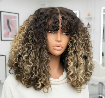 The mannequin showcases NuHaire's Honey Blonde Balayage Highlight Afro Kinky Curly Wig with Bangs, featuring a dark brown base with honey blonde highlights, a kinky curly texture, made from premium human hair, and designed with a glueless 5x5 lace.